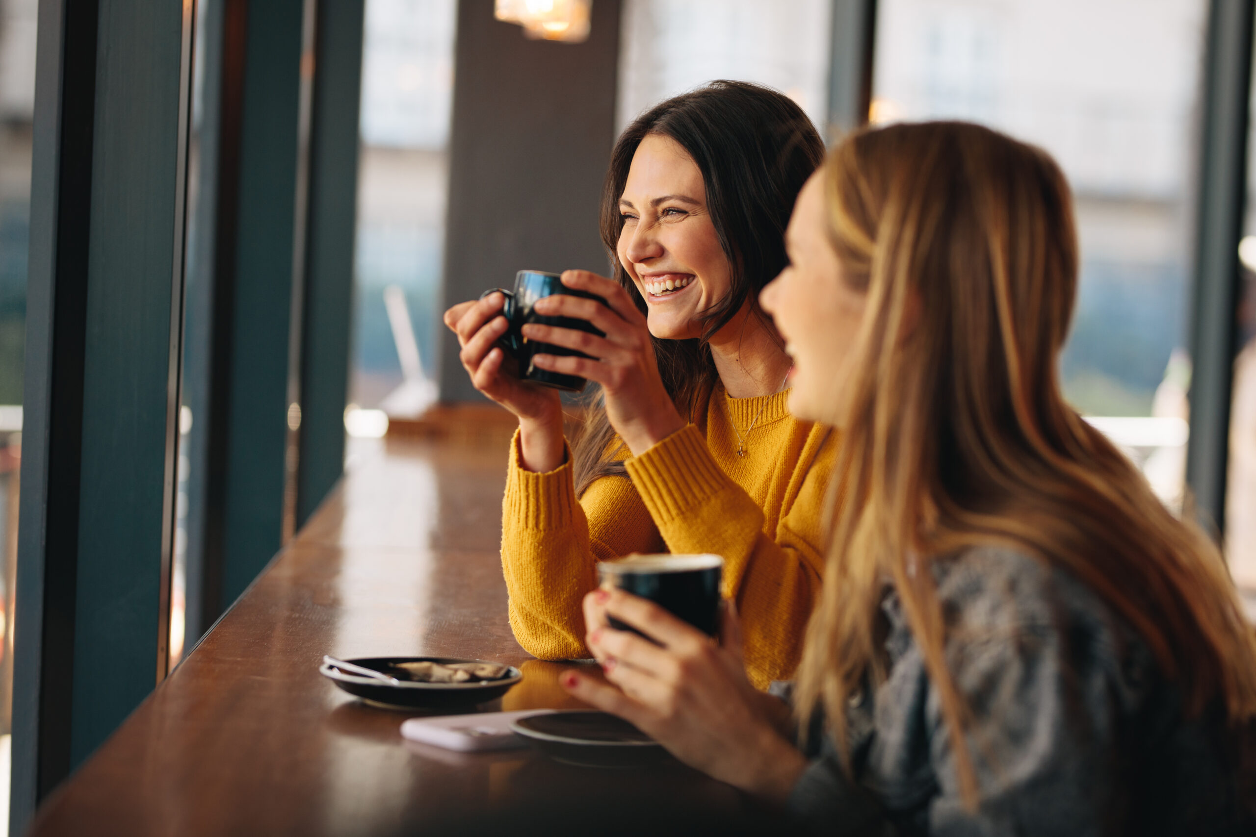Two women having coffee and smiling. Happy female friends having a great time together in a cafe.